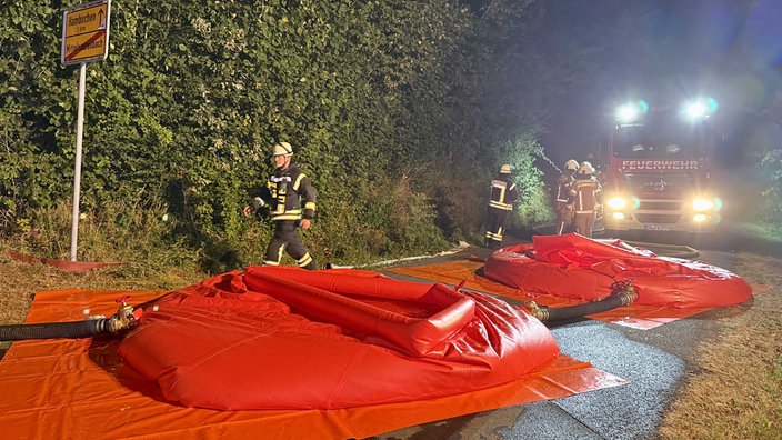 Die Feuerwehr befüllt nachts bei einem Einsatz zwei riesige, orangene Plastikbehälter, aus denen Einsatzkräfte Löschwasser entnehmen können.
