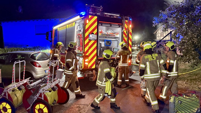 Mehrere Feuerwehrleute stehen nachts vor einem Einsatzfahrzeug und entnehmen diesem Löschschläuche.