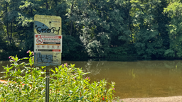 Ein mit Warnhinweis überklebtes Schild steht an einem Fluss