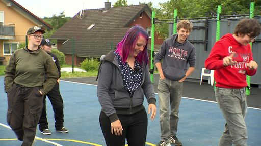 Eine Gruppe von jungen Menschen läuft lachend über einen Basketballplatz.
