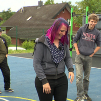 Eine Gruppe von jungen Menschen läuft lachend über einen Basketballplatz.