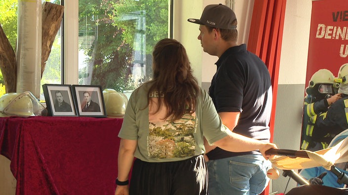 Martin Rick und seine Partnerin stehen vor einem Gedenkaltar mit zwei Schwarz-weiß-Fotos vor einem Fenster
