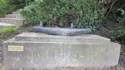 Der Boden einer abgesägten Bronze-Skulptur steht auf einem Stein-Sockel