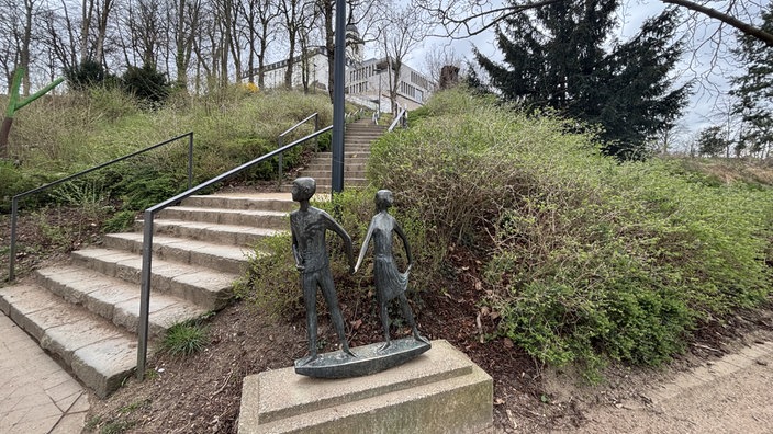 Eine Bronze-Skulptur steht auf einem Sockel vor einer Treppe am Michaelsberg