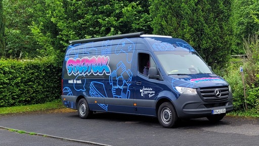 Ein Bus mit Design, das die Jugendlichen sich ausgedacht haben und Symbole für Essen, Spielen, Zusammenhalt und Austausch zeigt