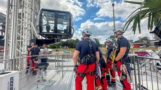 Mehrere Feuerwehrmänner der Höhenrettung stehen vor einem Fahrgeschäft auf der Düsseldorfer Rheinkirmes