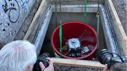Ein roter Ventilator wird an Seilen in einen Schacht abgelassen.