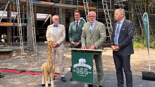 Vier Männer stehen hinter einem Podest mit der Aufschrift "165 Jahre Kölner Zoo"