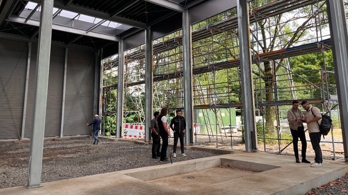 Fünf Personen stehen in einer Halle die sich im Aufbau befindet