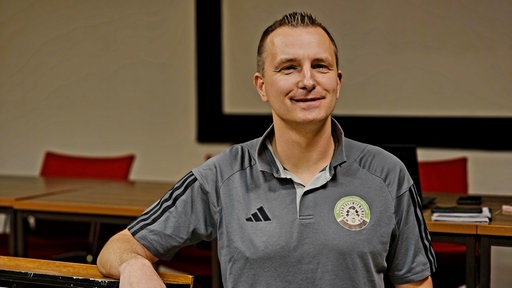 Gregor Hoffmann sitzt in Trikot-Shirt an einem Tisch und lächelt in die Kamera.