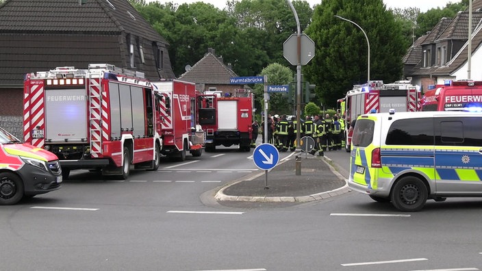 Zahlreiche Feuerwehr- und ein Polizeiwagen stehen in einer Straße in Übach-Palenberg, dazwischen stehen Einsatzkräfte.