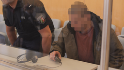 Der Angeklagte sitzt neben einem Justizbeamten.