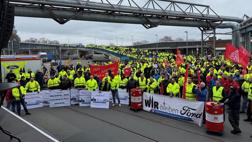 Mehrere hundert Menschen stehen versammelt vor einer Bühne. Es weht ein Banner der IG Metall