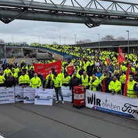 Mehrere hundert Menschen stehen versammelt vor einer Bühne. Es weht ein Banner der IG Metall