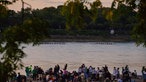 Viele Zuschauer im Rheinpark sehen die Mannschaften des Ruderrennens beim Zieleinlauf. Mit wichtigen Infos werden sie über die Lautsprecher versorgt. 