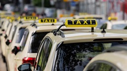 Mehrere Taxen stehen hintereinander in Reihe mit Taxisignalschild auf dem Autodach