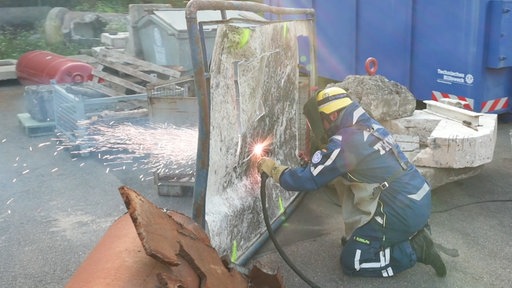 Ein THW-Mitarbeiter brennt in Schutzkleidung ein Loch in eine Metallwand.