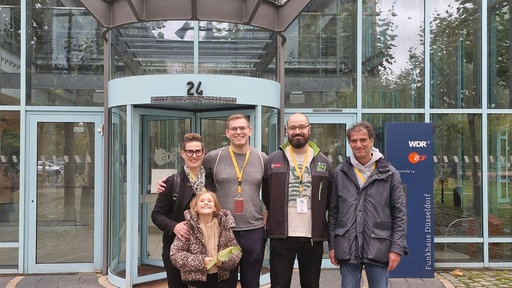Eine Gruppe von fünf Menschen steht vor dem Funkhauseingang