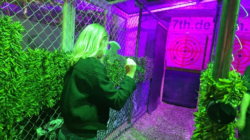 Unter Neonlicht wirft eine Frau mit blonden Haaren eine Axt auf eine Holzzielscheibe