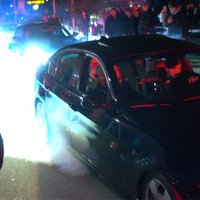 Zwei Autos hintereinander auf einer Straße. Am Rand stehen viele Menschen. 