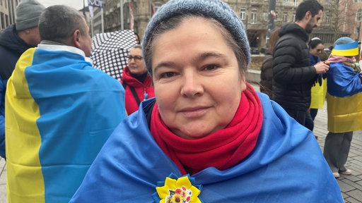 Eine Frau steht auf der Demo und hat eine Ukraine-Fahne um die Schultern gehängt 