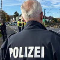 Ein Polizist steht mit dem Rücken zur Kamera. Im Hintergrund ist ein Bahnübergang dort sind weitere Polizisten und ein Einsatzfahrzeug.