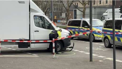 Zu sehen ist der Unfallort, bei welchem unter einem weißem LKW ein E-Scooter liegt.