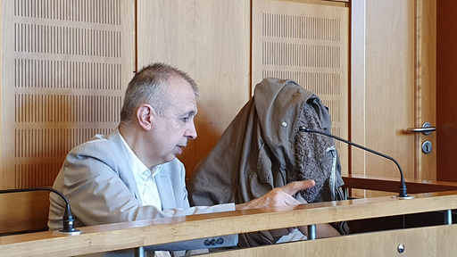 Der Verteidiger sitz im Gerichtssaal und gestikuliert mit der Hand.