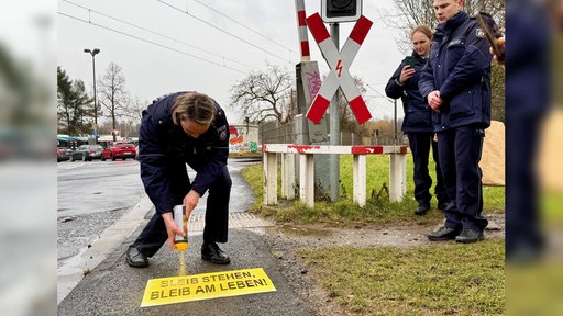 Eine Beamtin sprüht das Motto auf den Boden vor einem Bahnübergang.