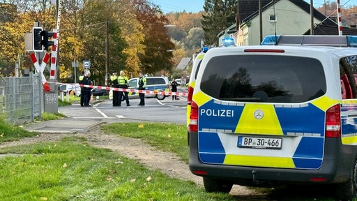 Polizeiwagen vor abgesperrtem Bahnübergang. Im Hintergrund stehen Polizisten.