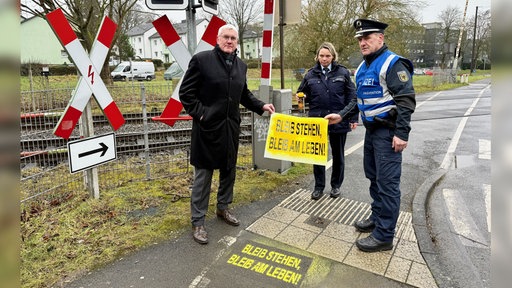 Landrat Sebastian Schuster (l.) und die Polizei stehen mit der Motto-Schablone vor einem Bahnübergang.