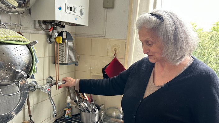 Das Bild zeigt eine Frau an einer Spüle in einer Küche
