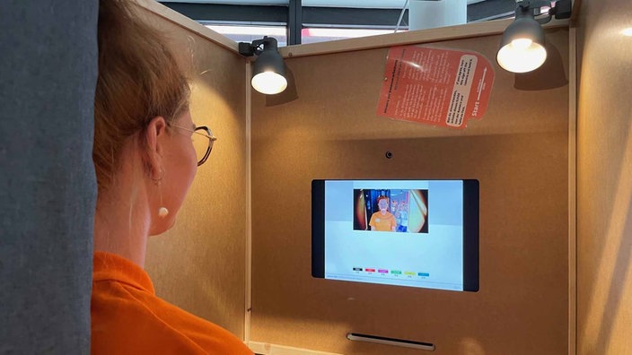 Eine Frau steht in einer Wahlkabine und wählt mit Gesichtserkennung