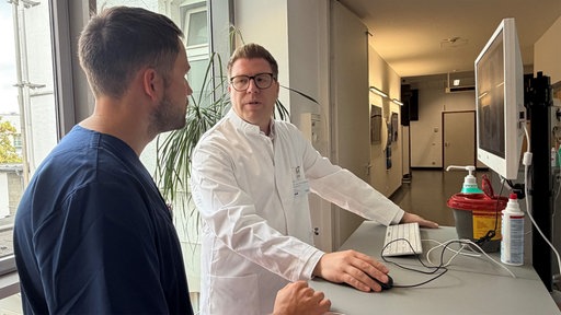 Zwei Männer unterhalten sich, einer trägt einen weißen Kittel