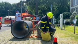 Eine Feuerwehrfrau in voller Ausrüstung kommt mit einem Kanister in der Hand aus einem Tunnel gekrochen