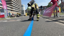 Eine Feuerwehrfrau in voller Ausrüstung rollt einen blauen Schlauch auf