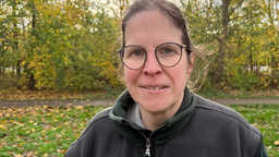 Eine Frau steht vor einem Waldabschnitt und schaut in die Kamera 