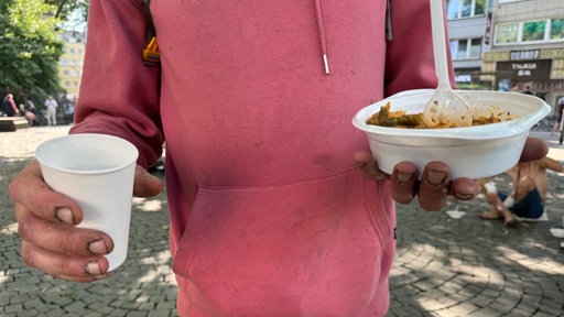 Mann hält einen Becher Wasser und etwas zu Essen in seinen Händen.