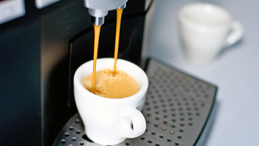 eine weiße Kaffetasse wird an einem Kaffeeautomaten befüllt
