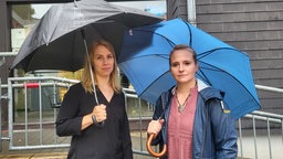 Zwei Frauen stehen vor einem Haus mit Regenschirmen