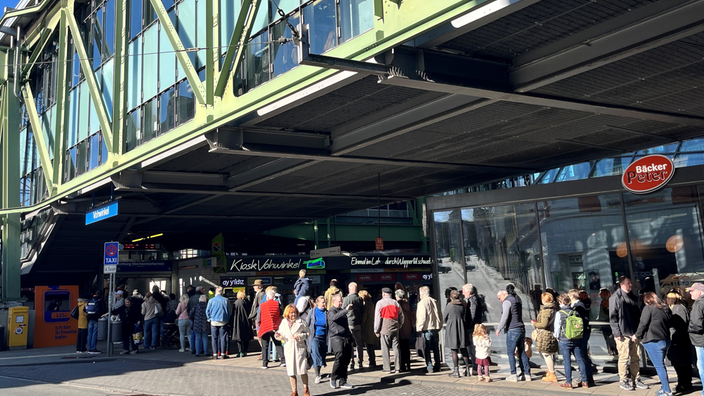 Viele Menschen stehen unterhalb einer Schwebebahn- Station in der Warteschlange bis auf die Straße.