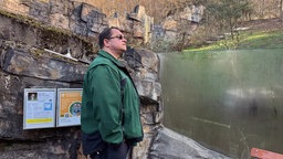 Tierpfleger in grüner Jacke steht am Tigergehege