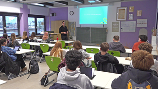 Klassenzimmer mit Schülern, Lehrer an der Tafel/ Projektion
