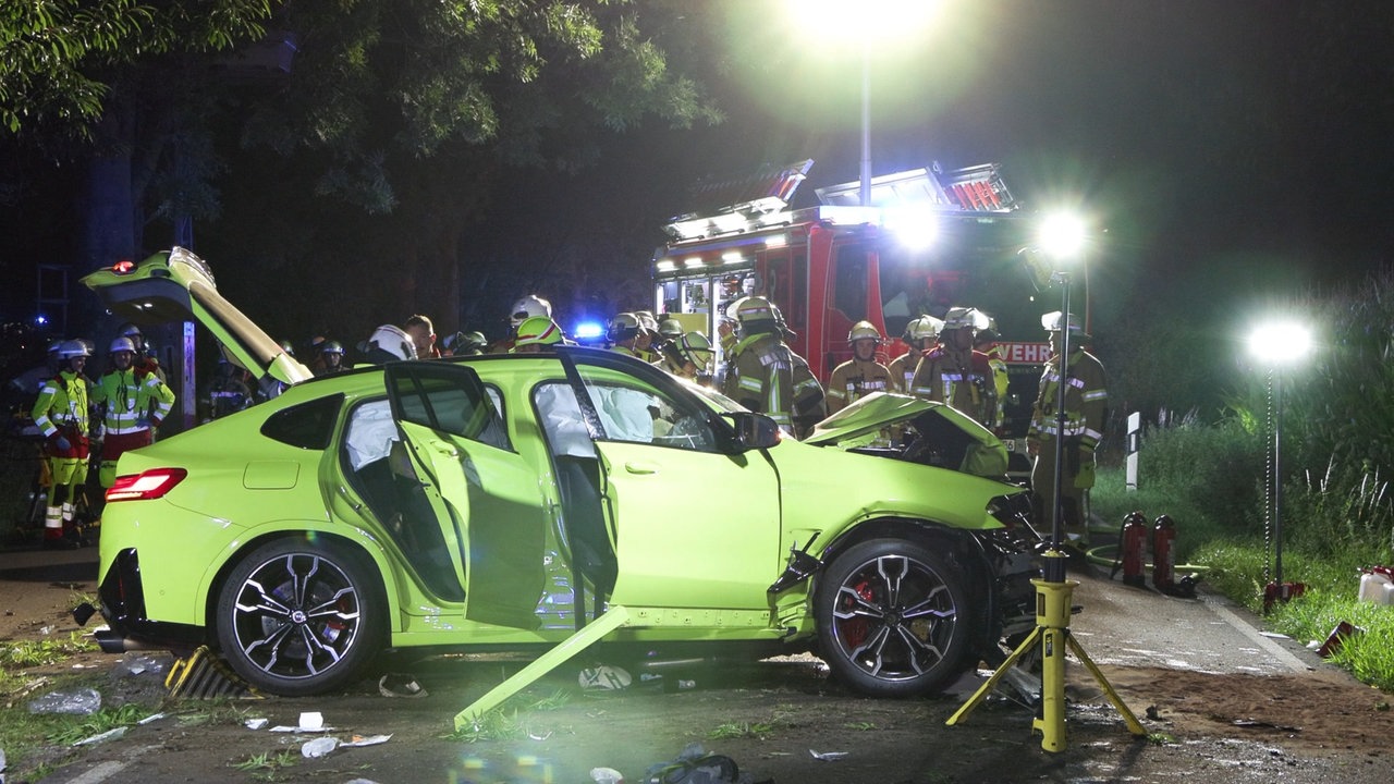 Im Vordergrund ein stark beschädigter grüner PKW, im Hintergrund Einsatzkräfte der Feuerwehr