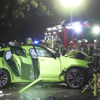 Im Vordergrund ein stark beschädigter grüner PKW, im Hintergrund Einsatzkräfte der Feuerwehr