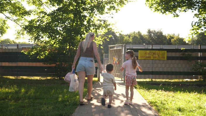 Das Bild zeigt eine Frau, die ihre Kinder in die Kita bringt. 