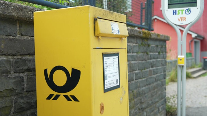 Ein gelber Briefkasten der Deutschen Post steht draußen vor einer Mauer.