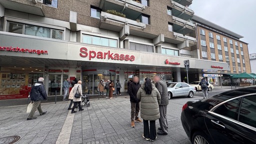 Vor der Sparkasse in Gelsenkirchen stehen Menschen und geparkte Autos
