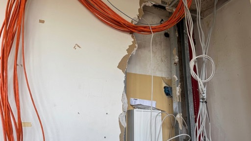Eine Wand in der Schule hat Löcher, Kabel hängen von der Decke. 
