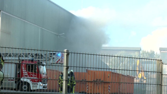 Eine Rauchwolke und Feuerwehrleute vor der Sperrmüll-Lagerhalle in Bochum beim Großbrand am 5. August 2025